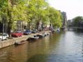 Houses, cars, bikes, trees and boats next to the canal..